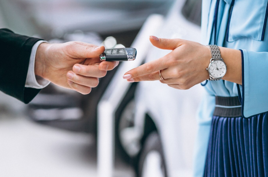 Close-up of a car key handoff between dealer and buyer, representing different vehicle ownership models including subscription, lease, and buying outright.