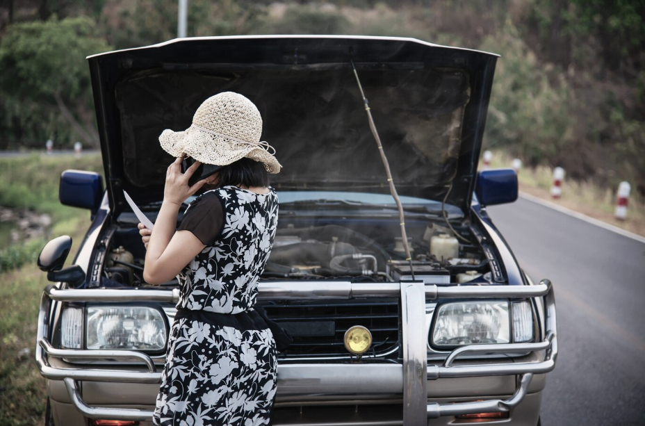 Woman calling for help next to broken down diesel pickup truck with smoking engine on roadside