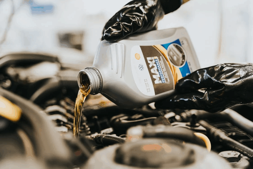 Person wearing black gloves pouring engine oil from a MAXI Performance container into a car engine during a DIY oil change at home.