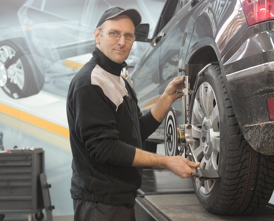 Auto technician performing wheel alignment and tire inspection on a lifted SUV in a garage setting