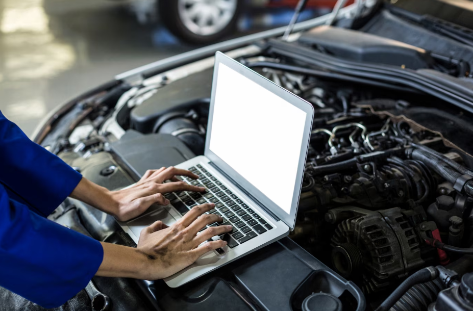 Mechanic using laptop to run predictive maintenance diagnostics on modern car engine in auto repair shop